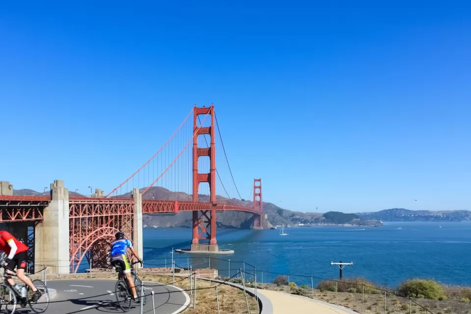 Two cyclists on a paved bike path overlooking the Golden Gate Bridge, San Francisco, California.